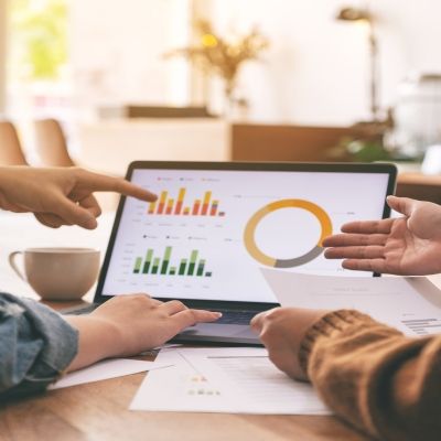 two people sat next to each other pointing at a laptop with bar graphs on