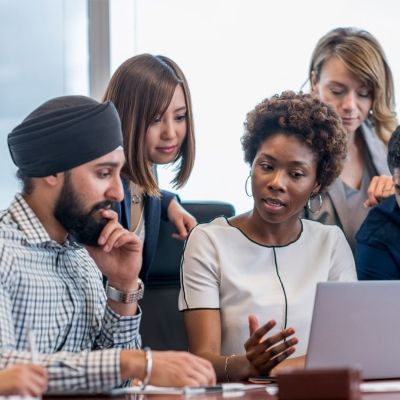 Diverse group of people sat looking at a laptop