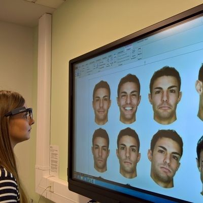A lady looking at a computer screen which has 9 male faces on