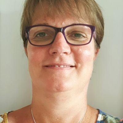 A head shot of a smiling Mariette Uys who has short hair and is wearing glasses