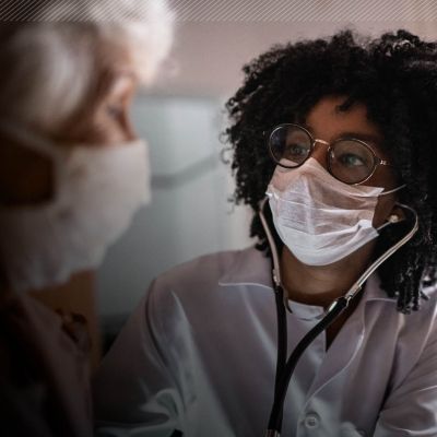 A nurse with a mask and glasses on attends to a patient