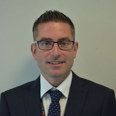 A head and shoulders shot of a smiling Paul Wheeler wearing glasses and a suit and tie looking directly into the camera