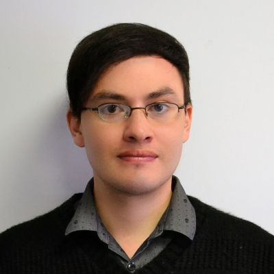 A head and shoulders shot of a smiling Adrian Guachalla wearing glasses, a shirt with a jumper looking directly into the camera