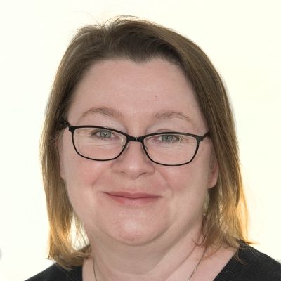 A head shot of a smiling Fiona Chalk wearing glasses stood face on looking directly into the camera