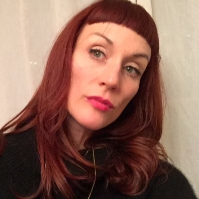 A head shot of a smiling Genevieve Maxwell wearing a black jumper stood face on with her head tilted to the left slightly looking into the camera