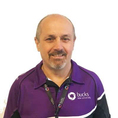 A head and shoulders shot of Philip Woodbridge wearing a BNU purple and black top with a BNU land yard around his neck facing directly into the camera