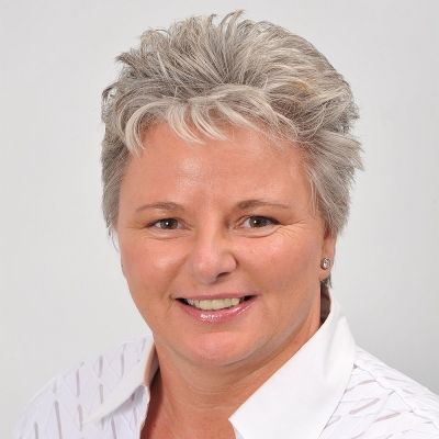 A head shot of a smiling Karen Buckwell Nut looking face on and directly into the camera wearing a white shirt