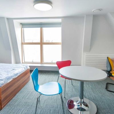 A bed, table, desk and chairs inside a Windsor House standard room accommodation