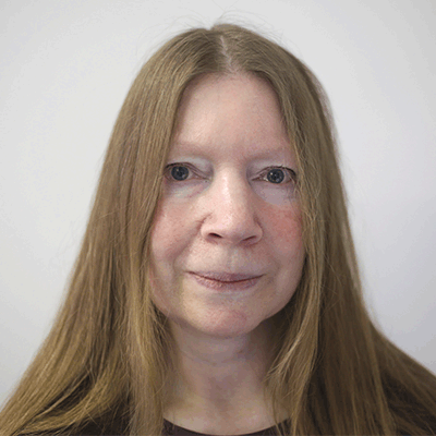 A head shot of a smiling Alison Tedman looking face on and directly into the camera, stood against a grey background