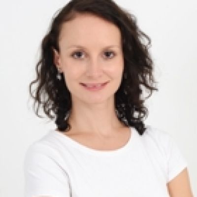 A head and shoulders shot of a smiling Lauren Vincent wearing a white t shirt stood against a white wall looking directly into the camera