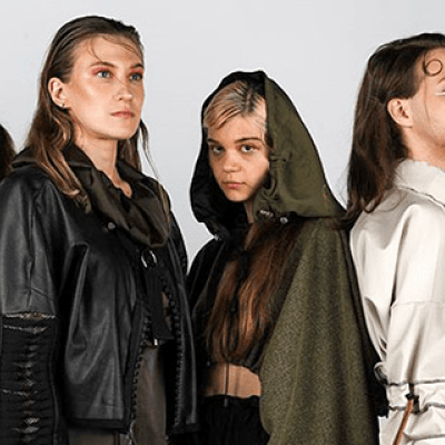 Four Fashion Design students stood posing back to back for a photoshoot against a grey wall