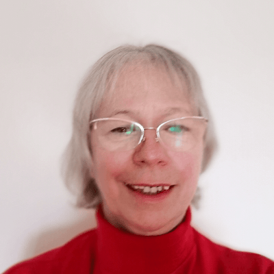 A head and shoulders shot of a smiling Christine Turney, who is looking directly into the camera wearing a red jumper and glasses