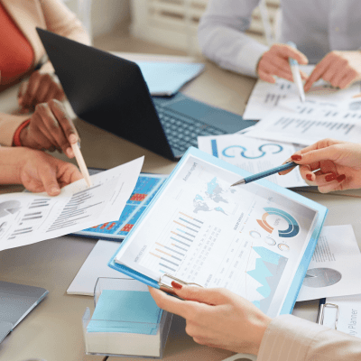 Data presented in bar charts and graphs on paper being held by people in a business meeting
