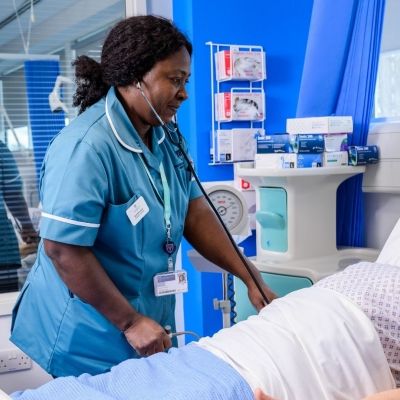 A Nursing student stood up leaning of a hospital bed which has a male dummy in it