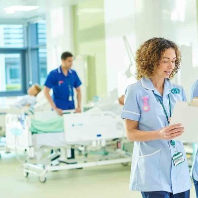 Two female nursing students looking at a clip board whilst walking through a hospital ward