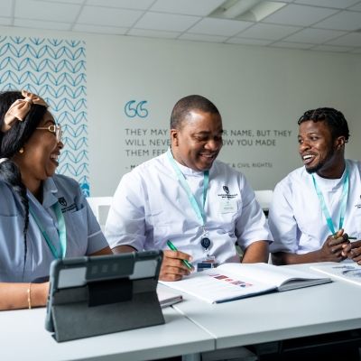 Three nursing students sat at a table next to one another looking at a textbook