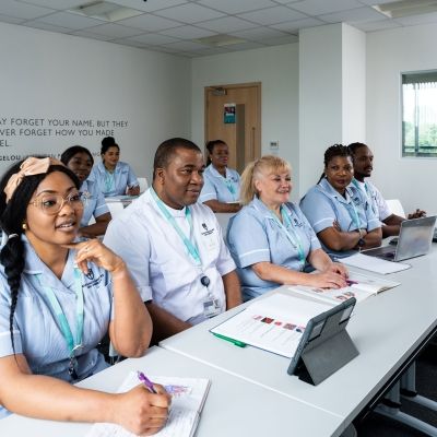 Eight nursing students sat in their uniform in a classroom facing the front of the room with textbooks open