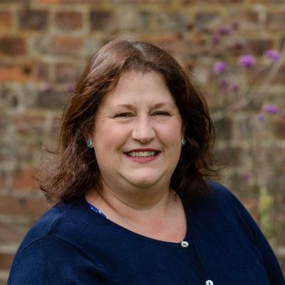 A head and shoulders photo of a smiling Beverley Griffiths, stood in front of a brick wall