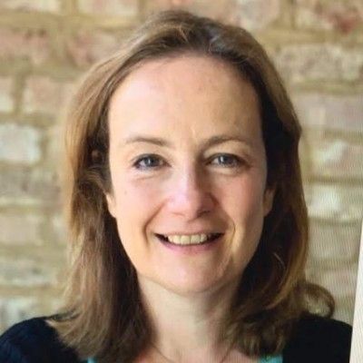A head shot of a smiling Catriona Craig wearing a blue top stood facing directly into the camera against a grey wall