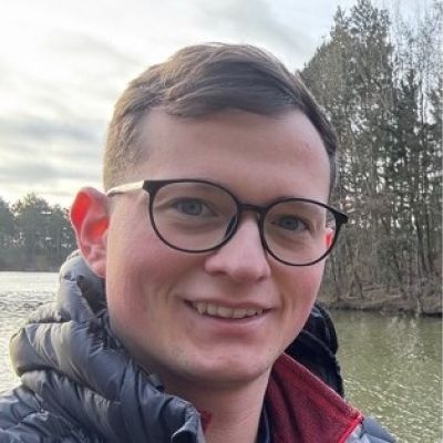 A headshot of BNU George Kingston-rayes wearing glasses stood in front of a lake.