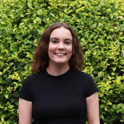 Woman in a black t-shirt in front of a hedge smiling
