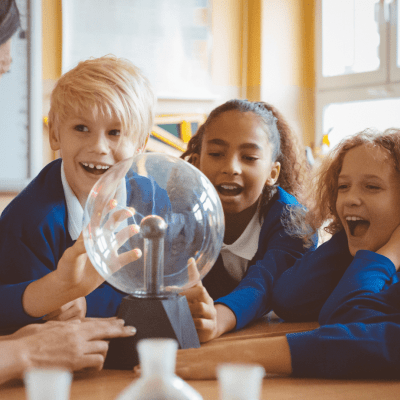 Four primary school children sat around a table smiling toward their teacher.