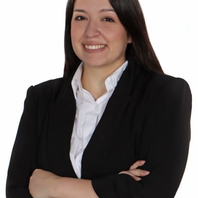 Student Debbie, who has tanned skin, long black hair, is wearing a black suit jacket and has her arms crossed