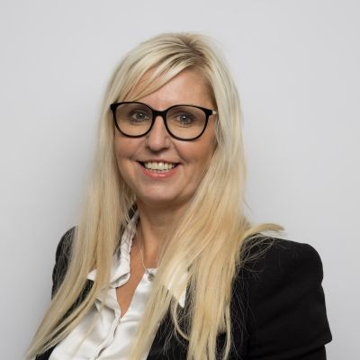 Photo of Tina, a white woman with long blonde hair who is wearing black spectacles and a white shirt.