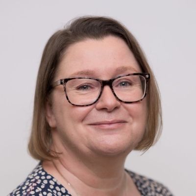 A head shot of a smiling Fiona Chalk wearing glasses stood face on looking directly into the camera