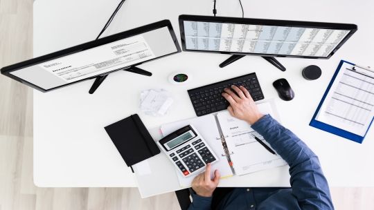 a birds-eye view of a person typing on a key board whilst looking at two screens