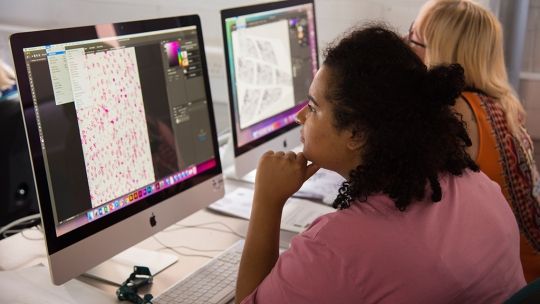 two female students sat looking at an Apple Mac computer