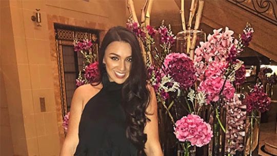 Nadina leaning on a table with large pink and purple flowers behind her