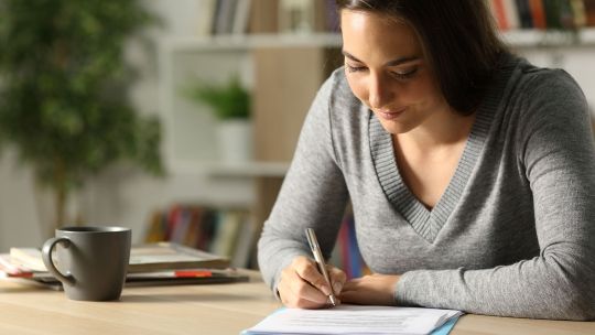 Woman sat at a table making notes on a bit of paper student writing studying