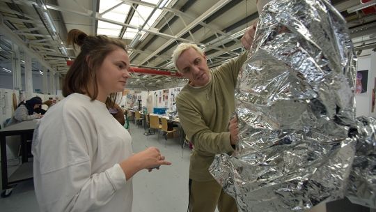 Two students look at a tin foil structure in the red shed