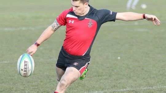 A rugby player kicking a rugby ball on a field