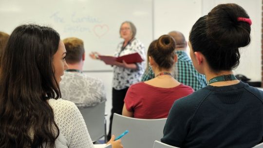 Two female students facing the front of a classroom sat on chairs