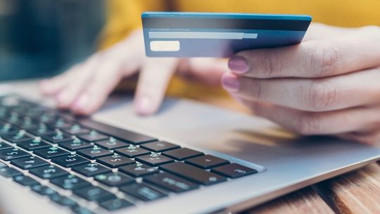 Someone holding a credit card in their left hand with their right hand on a laptop