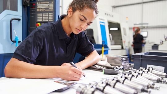 Female student engineer looking at paper work and writing with parts in front of her