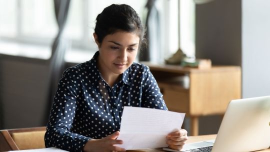 Student reading a piece of paper at a desk next to a laptop