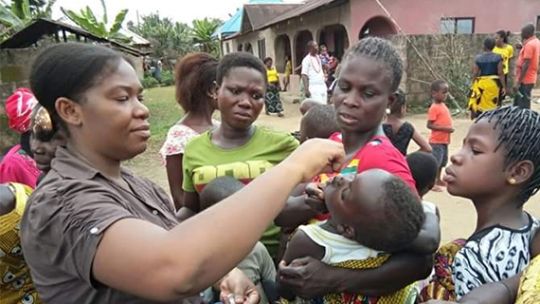 Mary Okuku as a nurse supporting a child who is being held in their mothers arms