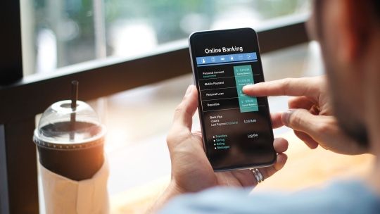 man using Online banking app on mobile phone while sitting down with coffee 
