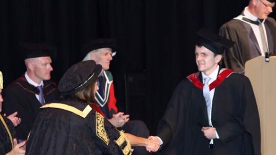 Robert Collcott shaking hands on the stage during his graduation ceremony
