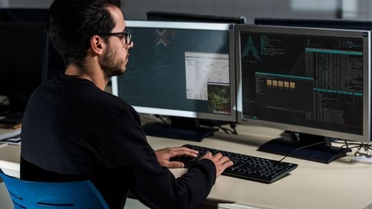 Man with glasses using linux software on computer at desk