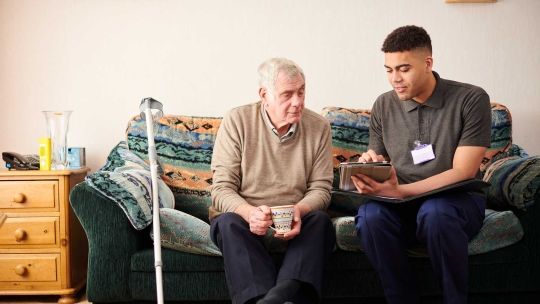 Senior man with crutch sitting with young male care worker