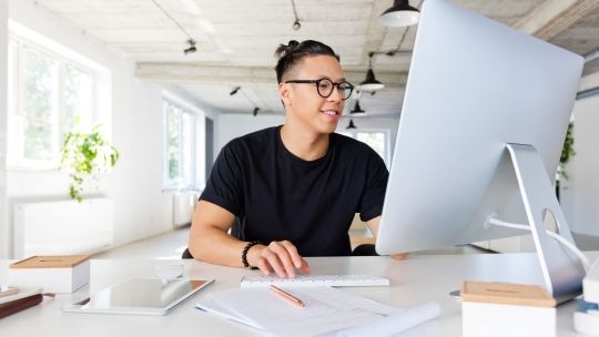 Student working on computer with paperwork around him.