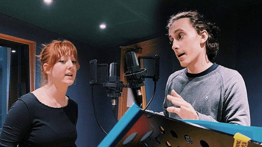 Two students singing opposite each other in a recording studio