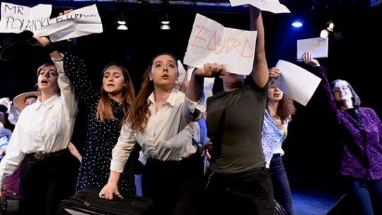 Performing arts students holding up bits of paper with names on looking defiant 
