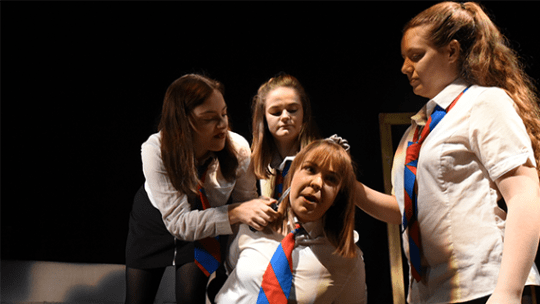 Three performing arts students in school uniform, hold another student hostage in a performance