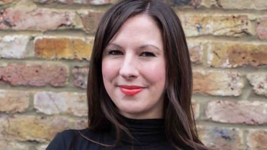 A head and shoulders shot of Lara Baker stood with her arms crossed wearing a black jumper and looking directly into the camera