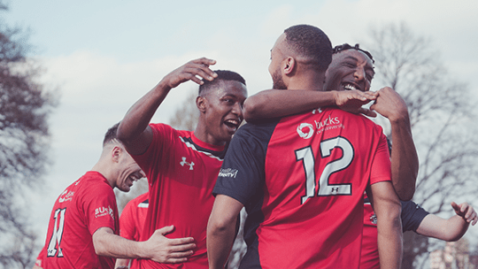 BNU football team celebrating by hugging one another after scoring a goal
